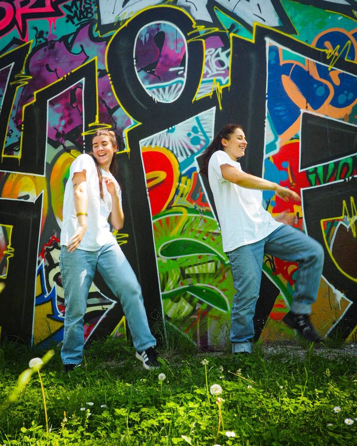 Deux membres du Cercle Hip Hop dansent en riant devant un mur couvert de graffitis