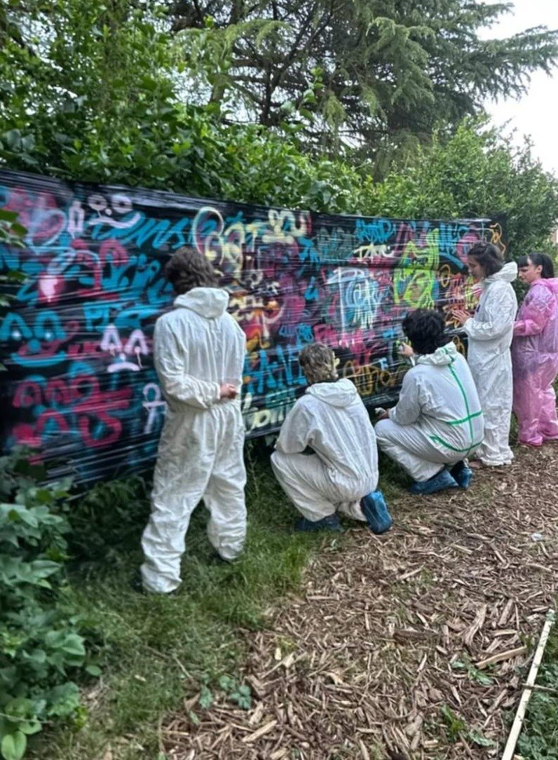 Atelier graff : des participants en combinaison taguent une bâche tendue dans un jardin