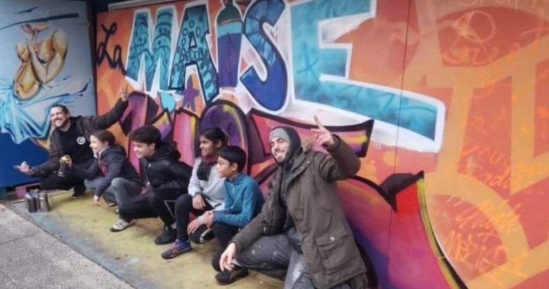 Les animateurs de La Maise et des enfants accroupis devant une fresque au nom du collectif